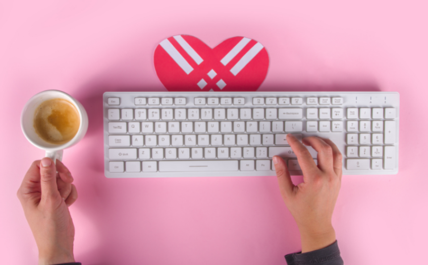 Person typing on a keyboard with a coffee and heart cut out on the desk